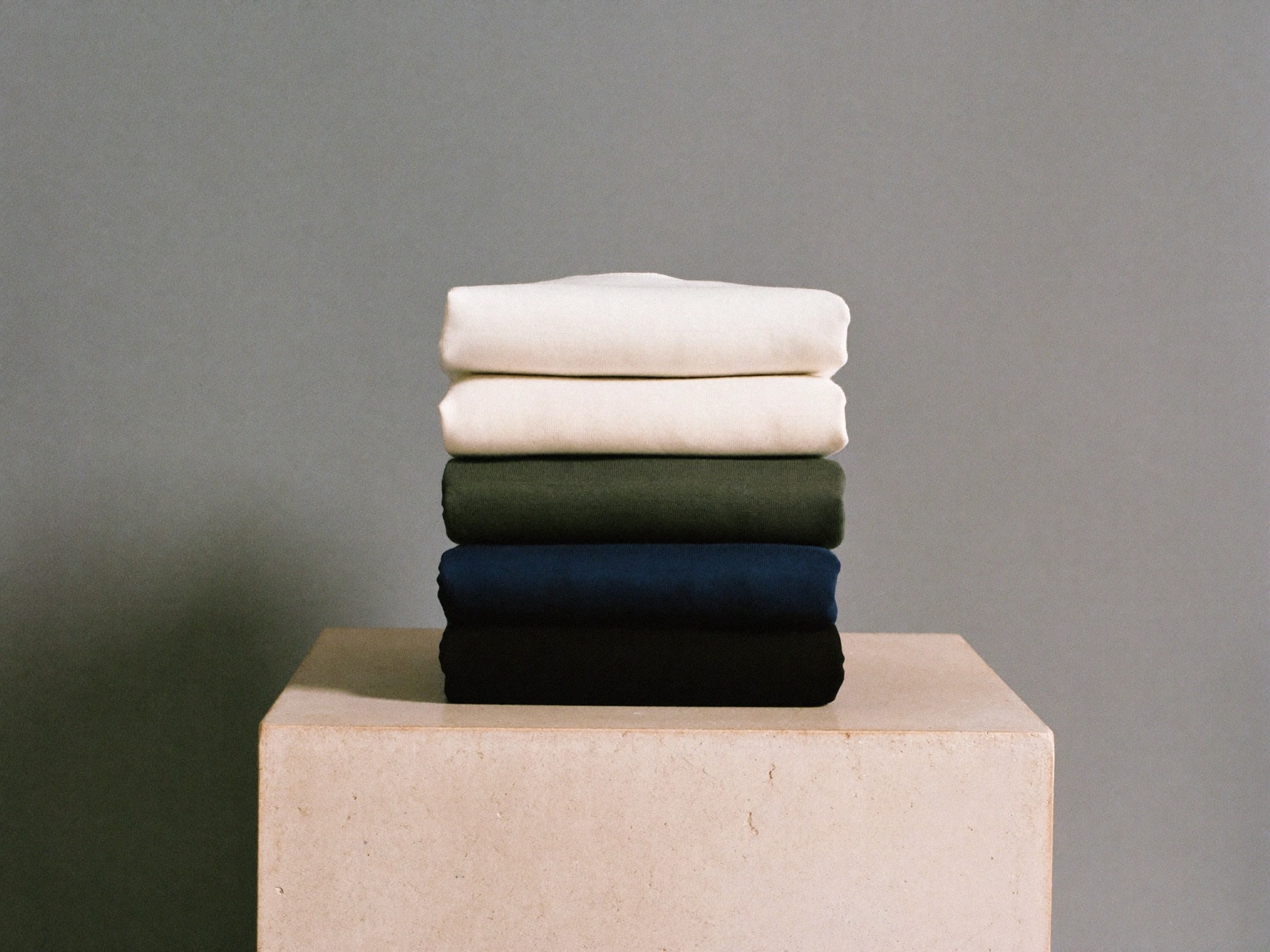 The five colourways folded in a stack — white, écru, olive, marine, noir